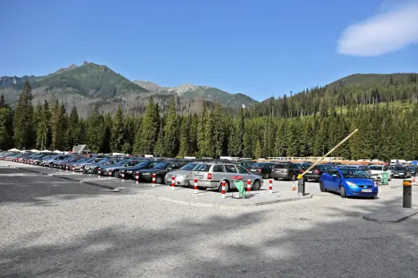 Parking pod Morskim Okiem, pełen samochodów, z górami i lasem w tle.