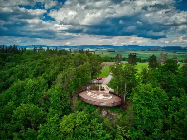 Widok na taras widokowy w otoczeniu lasu, z panoramą pól i gór w tle. Jakby to było jezioro wśród gór stołowych.