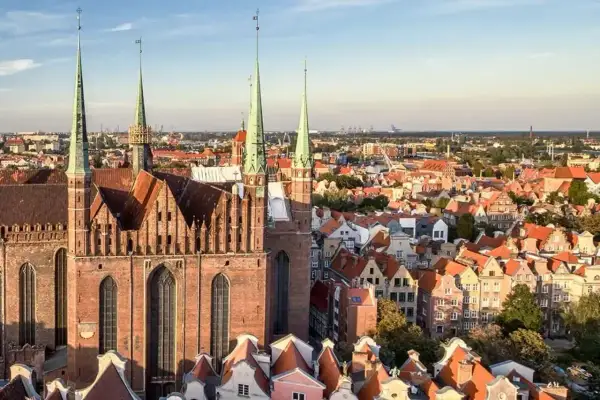 Widok na Bazylikę Mariacką i urokliwe kamienice Gdańska Stare Miasto. Dachy w odcieniach czerwieni i pomarańczy tworzą malowniczy krajobraz.