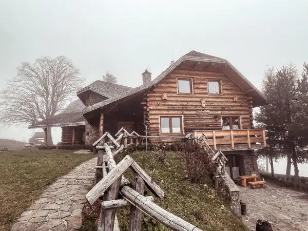 Drewniany dom z kamienną podstawą, kamienista ścieżka i płot. Mglisty dzień dodaje uroku temu miejscu, które oferuje liczne laskowa atrakcje.