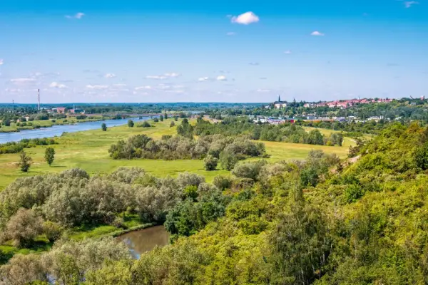 Krajobraz z rzeką, zielonymi wzgórzami porośniętymi drzewami i miastem w oddali.