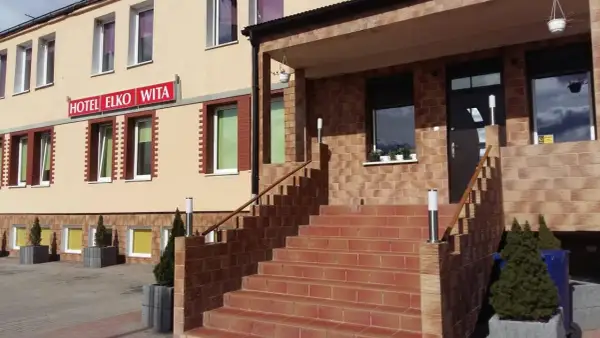 Wejście do hotelu Elko Elbląg. Schody prowadzą do drzwi, a nad nimi widnieje czerwony szyld.