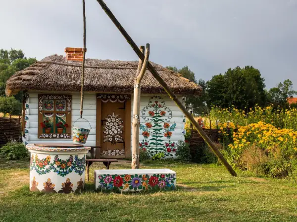 Malowana chata z łubą i studnią, ozdobiona kwiatami. Warto zobaczyć Zalipie i okolice, by podziwiać ludową sztukę.