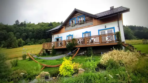 Dom z werandą i hamakiem w otoczeniu zieleni, idealne miejsce na wypoczynek w Bieszczadach.