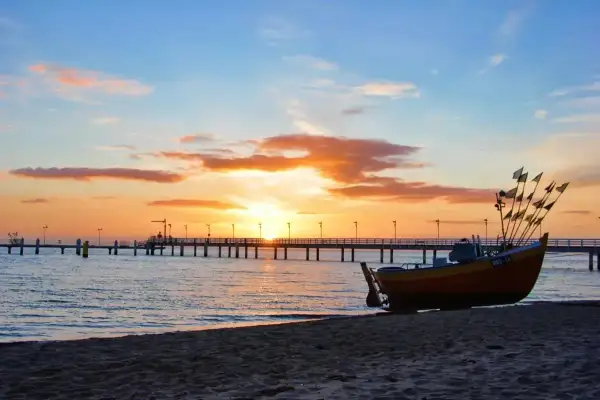 Łódź na plaży o zachodzie słońca, z molo w tle. Idealne miejsce, by zapytać, gdzie najbliżej nad morze z łodzi.