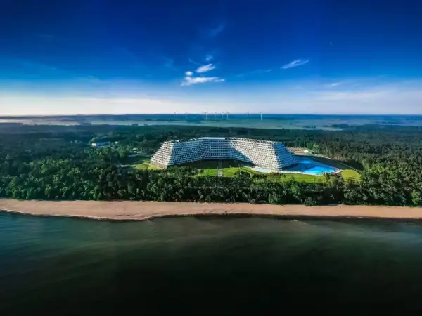 Gołębiewski nad morzem, z basenem i plażą, otoczony lasem, na tle wiatraków i błękitnego nieba.