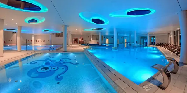 Nowoczesny aquapark w Ustce z basenami, jacuzzi i kolorowym oświetleniem. Na dnie jednego z basenów widnieje mozaika z ośmiornicą.