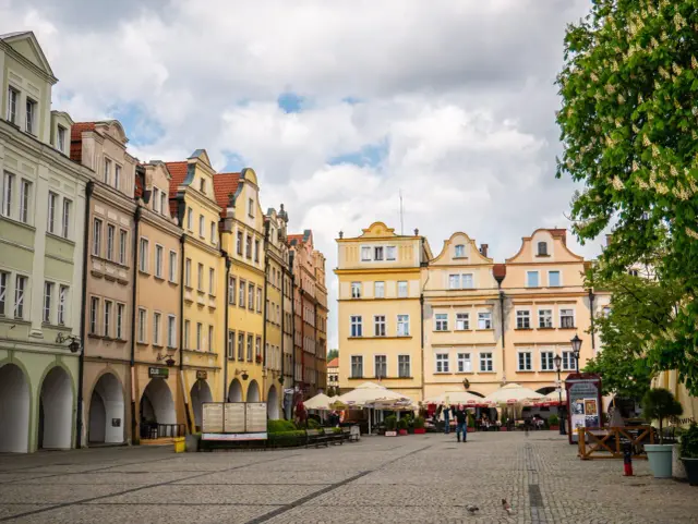 Kolorowe kamienice na starówce Jeleniej Góry, z arkadami i kawiarnianymi ogródkami, tworzą urokliwy plac.