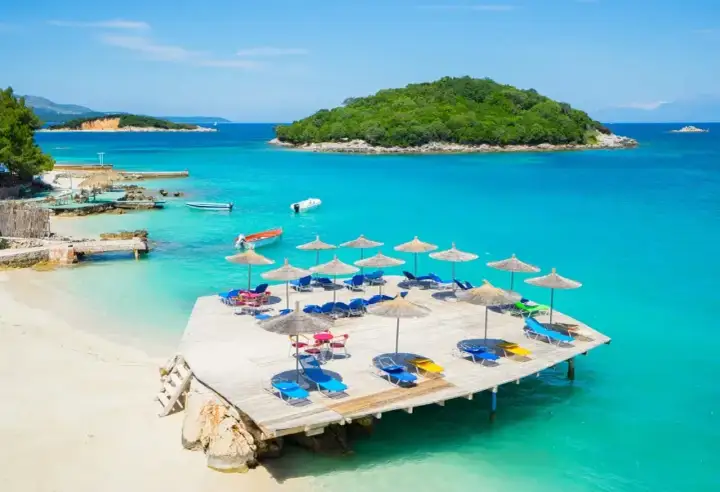 Rajska plaża w Albanii. Turkusowe morze, piaszczysta plaża, drewniany taras z leżakami i parasolami.