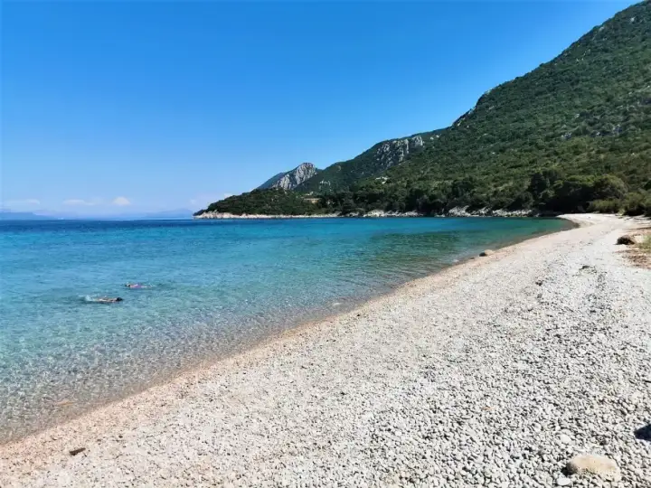 Chorwacja jakie morze? Turkusowa woda, kamienista plaża i zielone wzgórza. Dwie osoby pływają w krystalicznie czystej wodzie.
